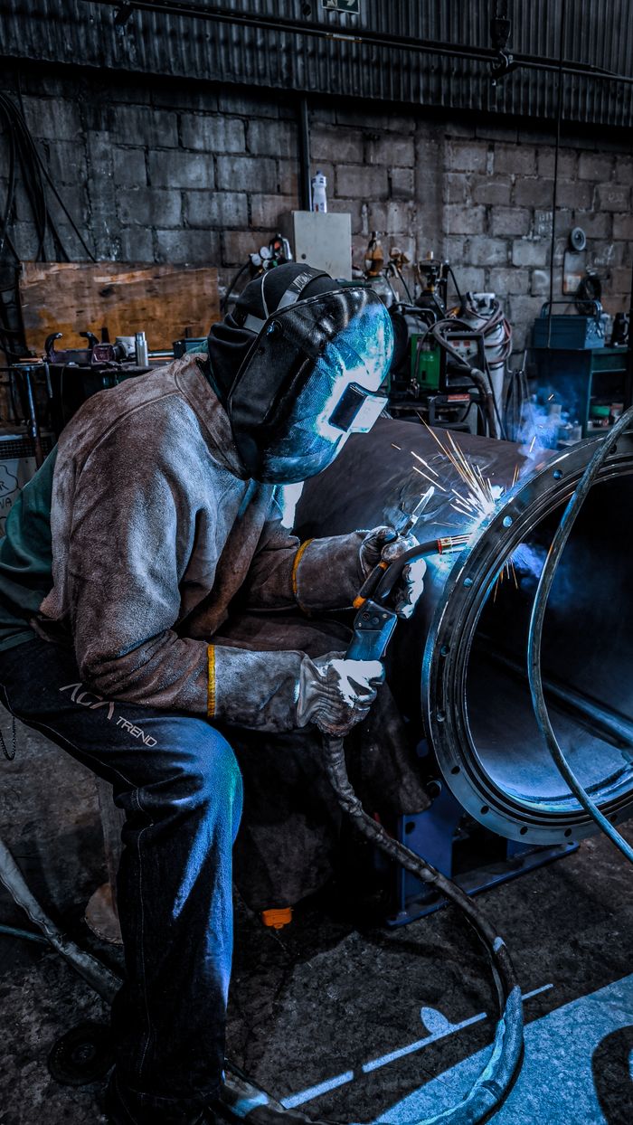 A worker welding inside a factory in Brazil, wearing safety gear and helmet.