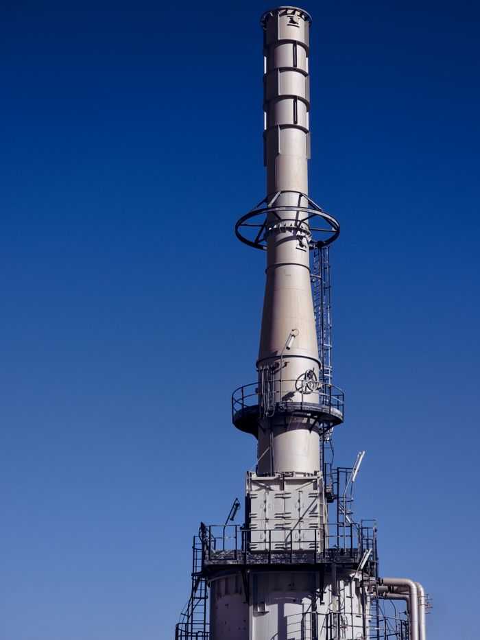 A tall industrial chimney with metal scaffolding against a clear blue sky, symbolizing energy production.
