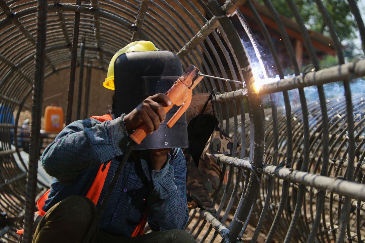 A construction worker welds steel rods on-site, showcasing industrial safety and skill.