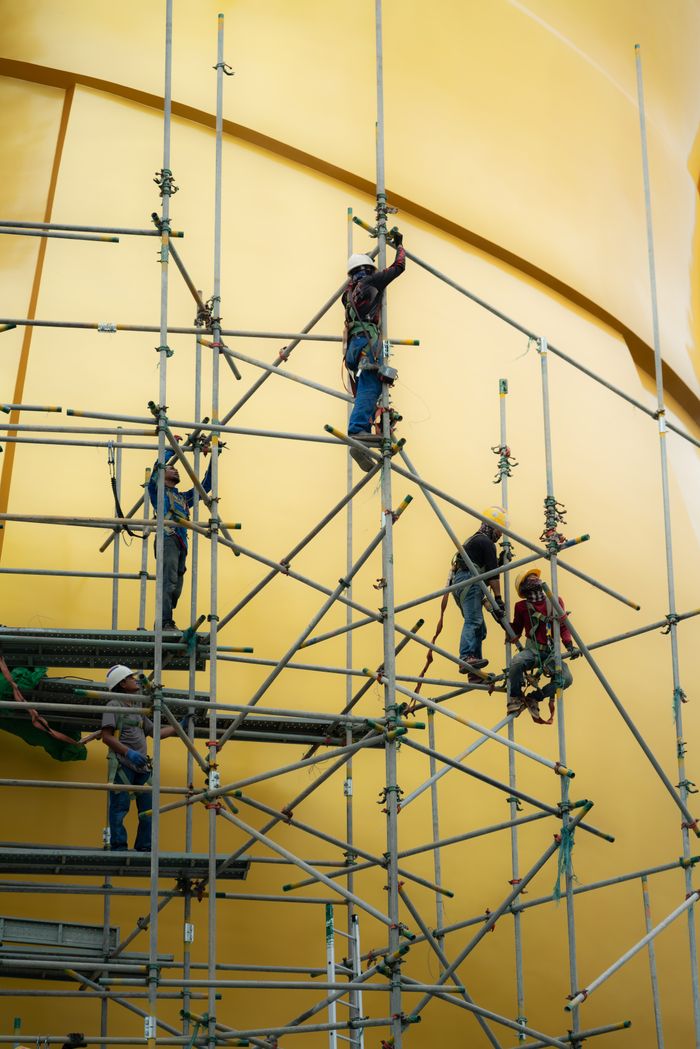 Construction workers climb scaffolding on a large structure, showcasing teamwork and industrial effort.